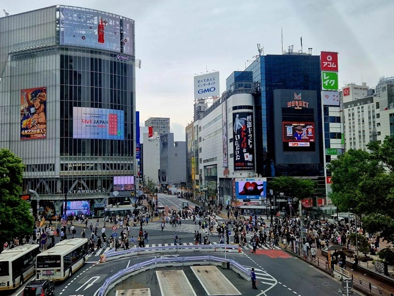 Multitud de peatones atravesando el famoso cruce de Shibuya en Tokio, rodeado de edificios y pantallas publicitarias.